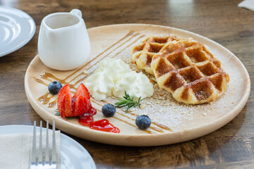 Deliciously waffles with whipped cream, strawberries and caramel syrup in the plate on wood table.
