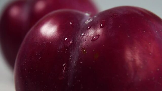 Drops of pure water fall on a ripe plum in slow motion. Macro shot