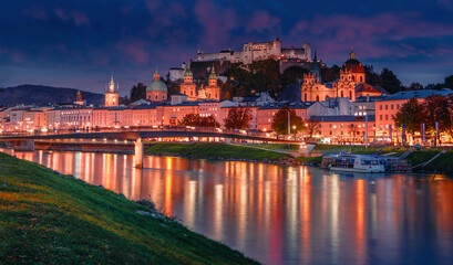 Obraz premium Wonderful evening scene of Salzburg city. View of the historical city, famous Hohensalzburg Fortress with reflection in the Salzach river, popular travel destination in Austria. Central Europe.