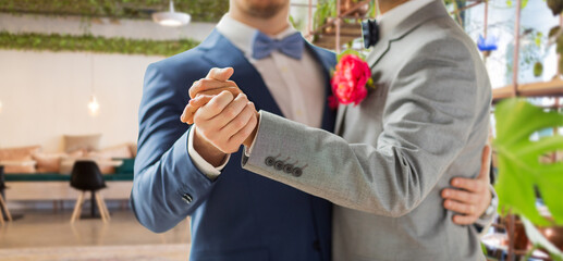lgbt, homosexuality and same-sex marriage concept - close up of happy male gay couple holding hands and dancing on wedding over restaurant background