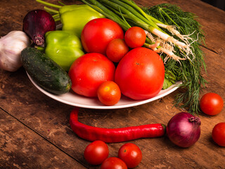 Fresh vegetables from the backyard in a plate and on a rustic table. Harvest fresh vegetables on the table - tomatoes, cucumbers, onions, peppers, garlic.