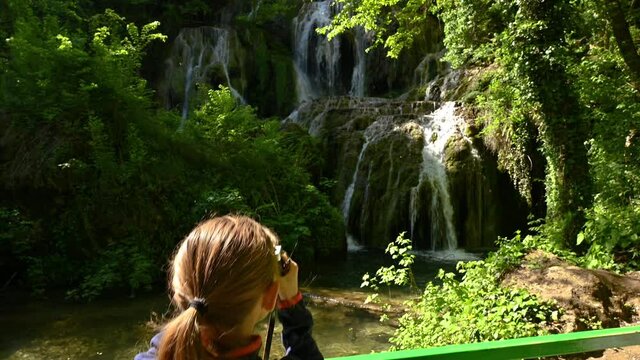 Video with a girl taking pictures and enjoys a beautiful waterfall in green spring forest, Krushuna falls, Balkan Mountains, Bulgaria..