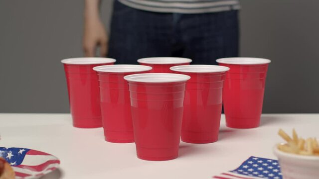 Sliding Shot Approaching Cups as Person In Background Drinks During Beer Pong Game