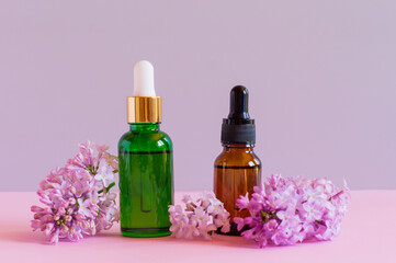 Mock up glass dropper bottles on a pink background with lilac flowers. Unbranded Cosmetic pipette serum.