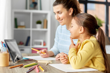 family, motherhood and leisure concept - mother spending time with her little daughter drawing with color pencils and using tablet pc computer at home