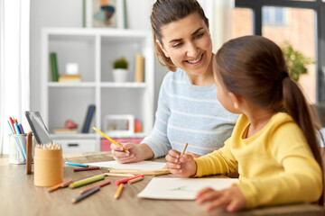 family, motherhood and leisure concept - mother spending time with her little daughter drawing with color pencils at home
