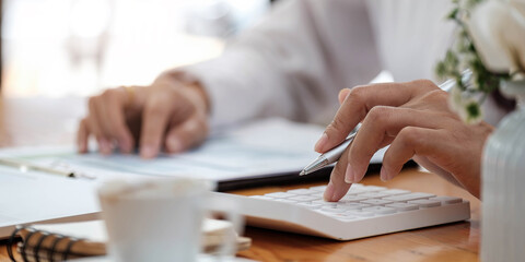 Close up Business woman using calculator and laptop for do math finance on wooden desk in office and business working background, tax, accounting, statistics and analytic research concept