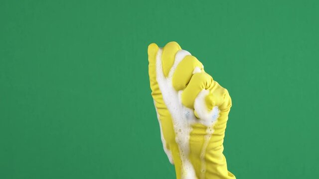 Woman hand in yellow protective rubber glove squeezes blue cleaning sponge over green background. 4k video