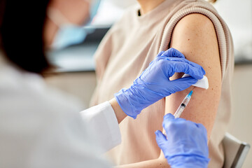 health, medicine and pandemic concept - close up of female doctor or nurse wearing protective medical gloves with syringe vaccinating patient at hospital