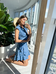 Fit tanned woman in blue summer dress and hat at home take photo selfie on phone in mirror for social media, stories, vertical