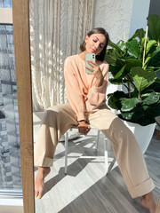 Fit tanned woman in peach sweater and classic beige trousers at home take photo selfie on phone in mirror for social media, stories, vertical