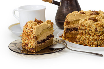 Partly cut sponge cake against cup and copper coffee pot