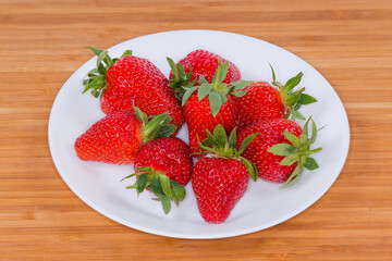 Fresh strawberries with tails on dish on the wooden surface