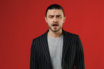 Obraz premium Young sad confused shocked surprised businessman latin man long hair ponytail wear black striped jacket grey shirt look camera with open mouth isolated on red background. Concept of people lifestyle.