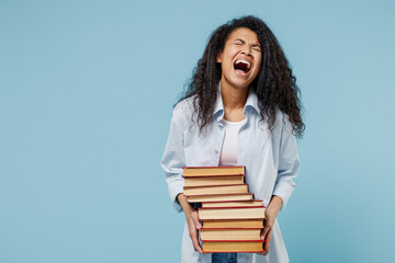 Young stressed shcoked african american girl teen student in denim clothes hold many hard books prepare for exam scream isolated on blue background Education in high school university college concept