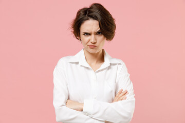 Fototapeta premium Young indignant frowning sad shrewd employee business woman corporate lawyer in classic formal white shirt work in office hold hands crossed isolated on pastel pink color background studio portrait