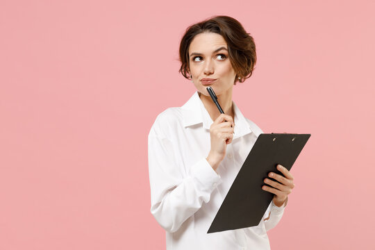 Young fun thoughtful successful employee business secretary woman corporate lawyer in classic formal white shirt work in office clipboard with papers write document isolated on pastel pink background.