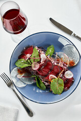 Beef jerky appetizer with lettuce, on a light background with a glass of wine. Brisaola with red beet leaves and red wine on a white tablecloth