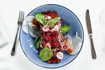 Bresaola on a blue plate with lettuce leaves, top view, serving beef jerky from the chef.