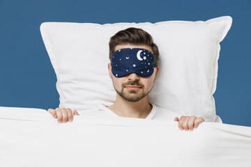 Young serious calm man 20s wear pajamas jam sleep mask rest relaxing at home with closed eyes lies...