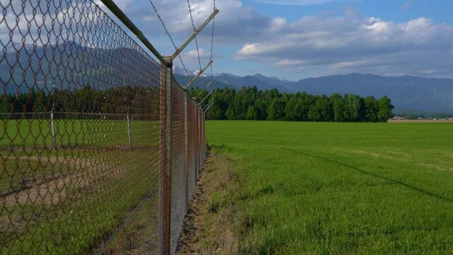 Security fence of Ljubljana airport in Slovenia. Barb wire fence. Alps mountains in the distance. Tilt up, wide angle