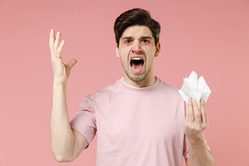 Shocked unhappy sick allergic man has watery red eyes runny nose suffer from allergy symptoms hold paper napkin raised hand up scream feel unhealthy isolated on pastel pink color background studio