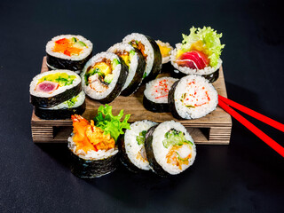 set of sushi rolls on wooden board on black background. different kind of maki sushi roll with tuna, salmon, eel, cucumber and avocado