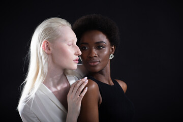 Caucasian albino girl and african american young woman hugging on black background. Women friendship, love and relationships concept.