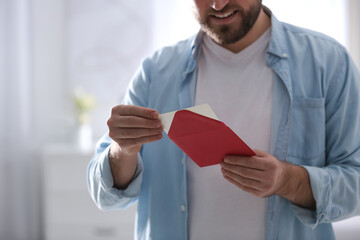 Man holding envelope with greeting card at home, closeup