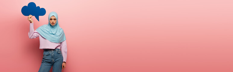 young muslim woman in blue hijab and jeans holding thought bubble on pink background, banner