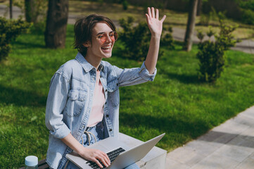 Young student freelancer copywriter friendly woman 20s in jeans clothes sit on bench in spring park...
