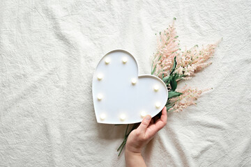 Hand with heart lightbox and wild flowers . Flat lay on off white textile. Natural materials, environment concious, low impact lifestyle. Pale pink Prachtspiere flower.