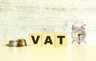 There are three wooden cubes with letters on the table next to the coins. The word VAT. On a gray background.
