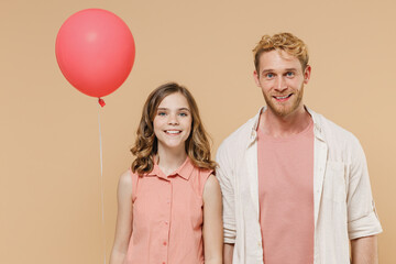 Young smiling cool parent man with child teen girl wear casual clothes Daddy kid daughter celebrate birthday party and hold red air inflated helium balloon look camera isolated on beige background