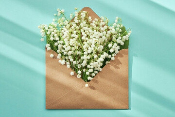 Open craft envelope with lilies of the valley on a turquoise background. The sun casts graphic shadows. Top view.