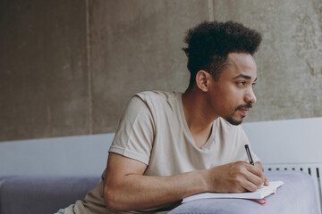 Side view creative introvert young artist student african american man 20s wear beige t-shirt sit...