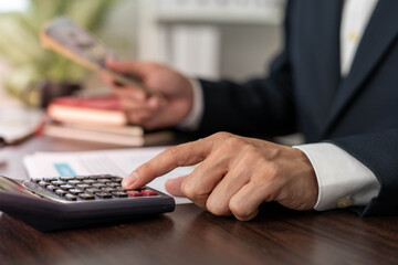 Businessman is pressing the calculator calculate the various costs that must be paid by the bill. Many invoices held and placed on the table