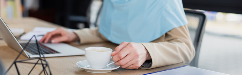 cropped view of muslim businesswoman near laptop and coffee cup in office, banner