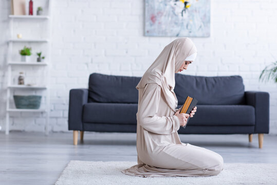 side view of muslim woman praying with koran on floor at home