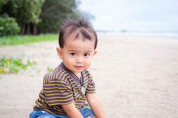 Cute child little boy 1 year old sitting on sand beach at coast. he was playing with fun in holidays with blur blue sea. tourist tropical travel ocean summer or happy family lifestyle vacatio concept.