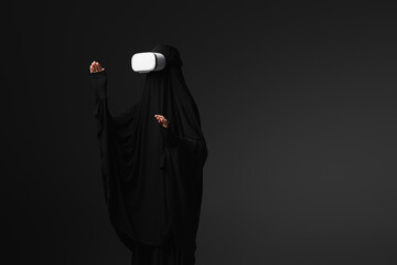muslim nun in black abaya gesturing in vr headset isolated on black