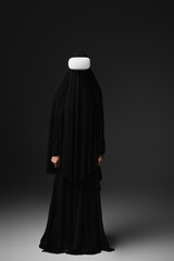 full length view of muslim nun in black abaya and vr headset on black background