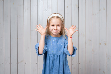 Positive little girl smiling happily and spreads her hands to the side, says - surprise