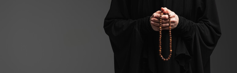 cropped view of muslim nun with rosary praying isolated on dark grey, banner