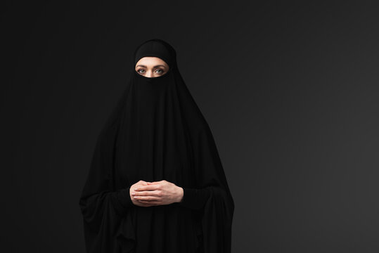arabian woman in black niqab and amaya looking at camera isolated on black