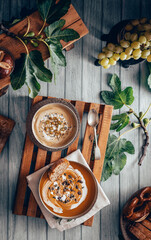 Flat lay photography of a vegan cream soup on a table of old wood. Top view of a puree of seasonal products on a wooden tray among fig leaves, bread and grapes with a vintage look.