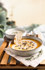 Food photography of a vegan pumpkin cream soup and bread with selective focus. Vegetables recipe. An autumn puree of seasonal products on a wooden table with vintage look.