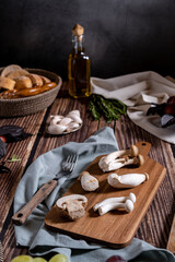 Dark photography of mushrooms, asparagus, bread, garlic and plums on a table of old wood. Vegetables recipe of for autumn or winter. Moody picture of seasonal cultivated fungus on a wooden table.