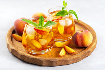 iced carbonated tea with peaches and mint in a glass on a gray background, horizontal
