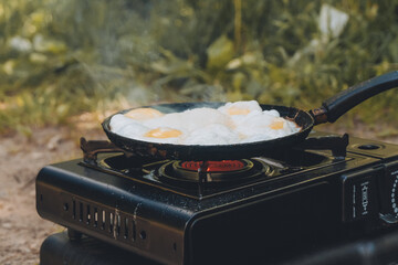 In a frying pan, eggs are fried on a gas burner, a camping gas stove on a summer day. Concept of...